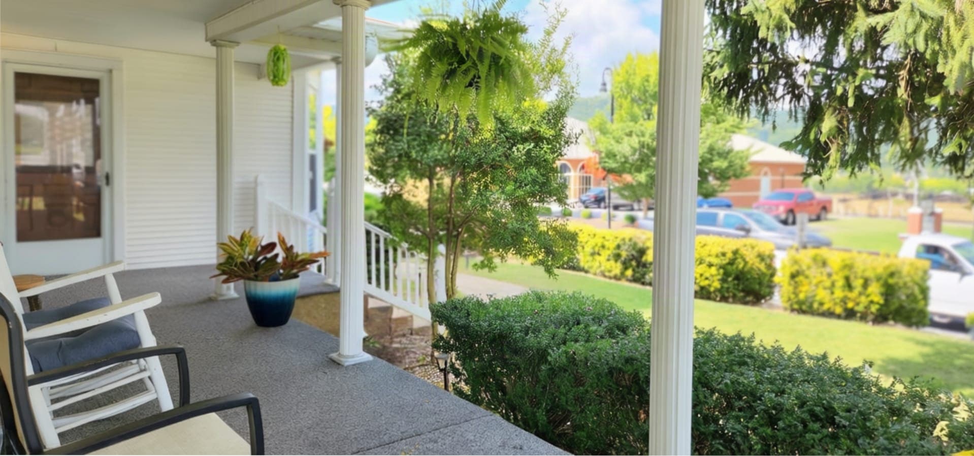 A porch with chairs, potted plants, and a view of a suburban street.