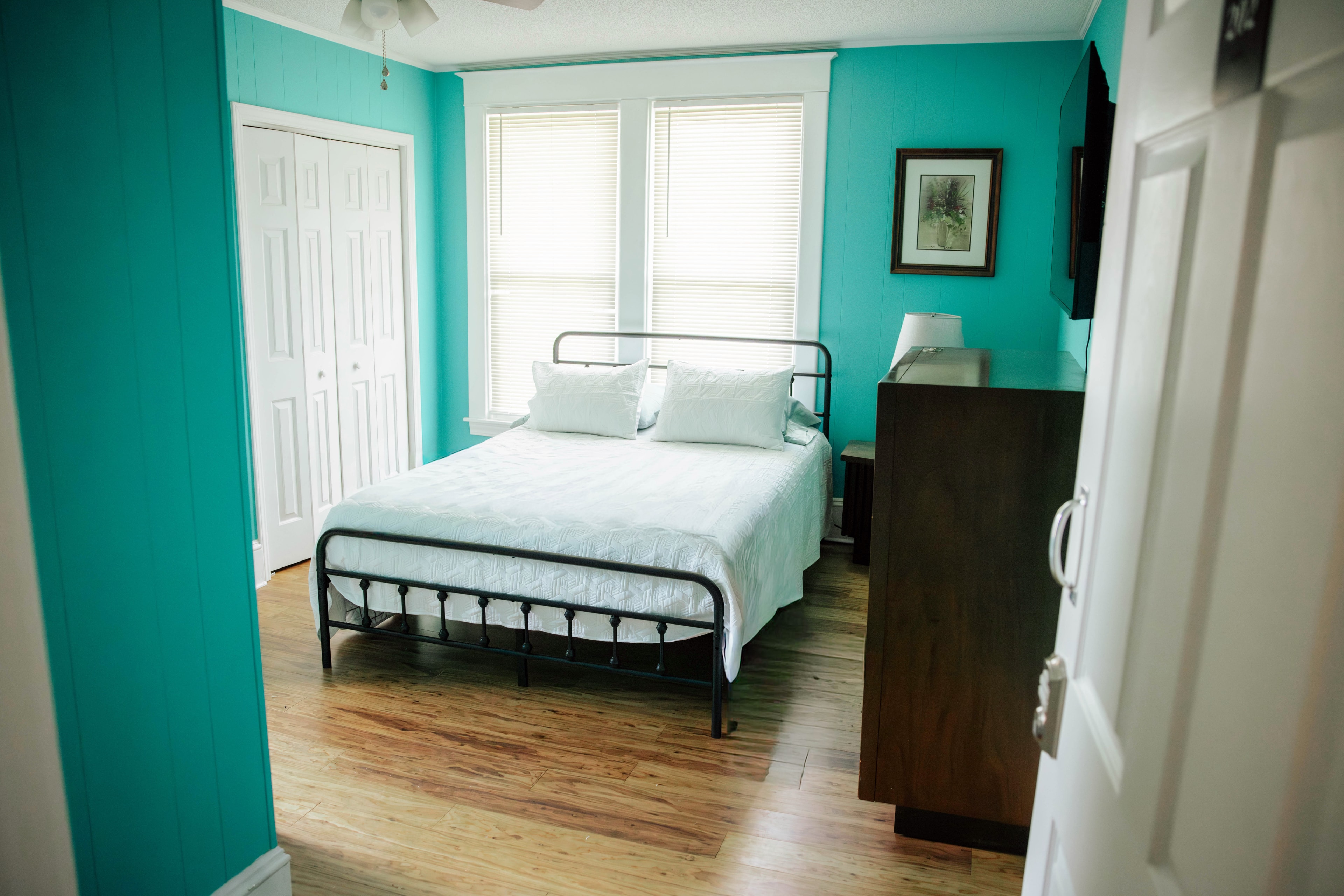 A cozy bedroom featuring a metal-framed bed, turquoise walls, and wooden flooring.