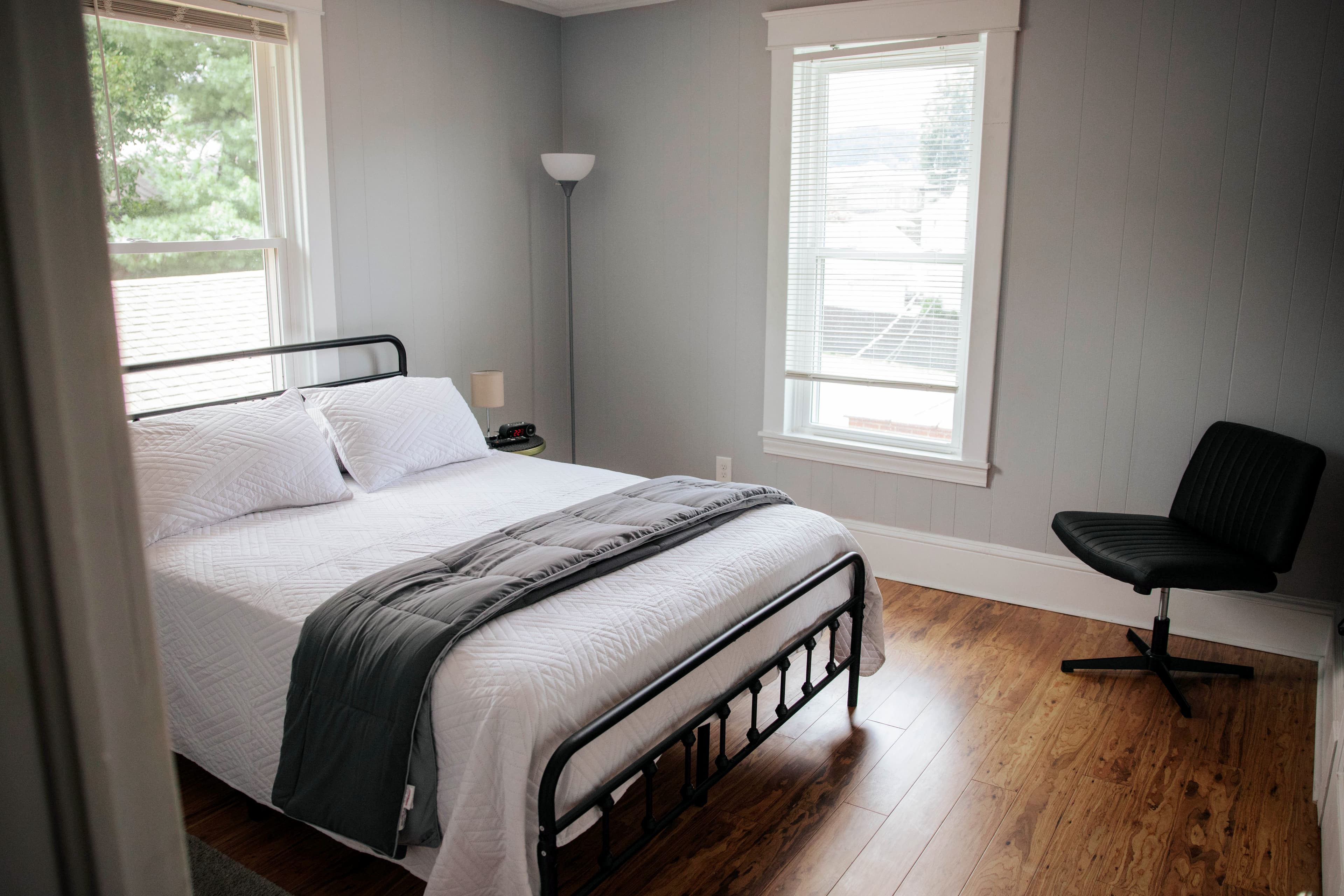A minimalist bedroom featuring a double bed, a chair, and large windows with natural light.