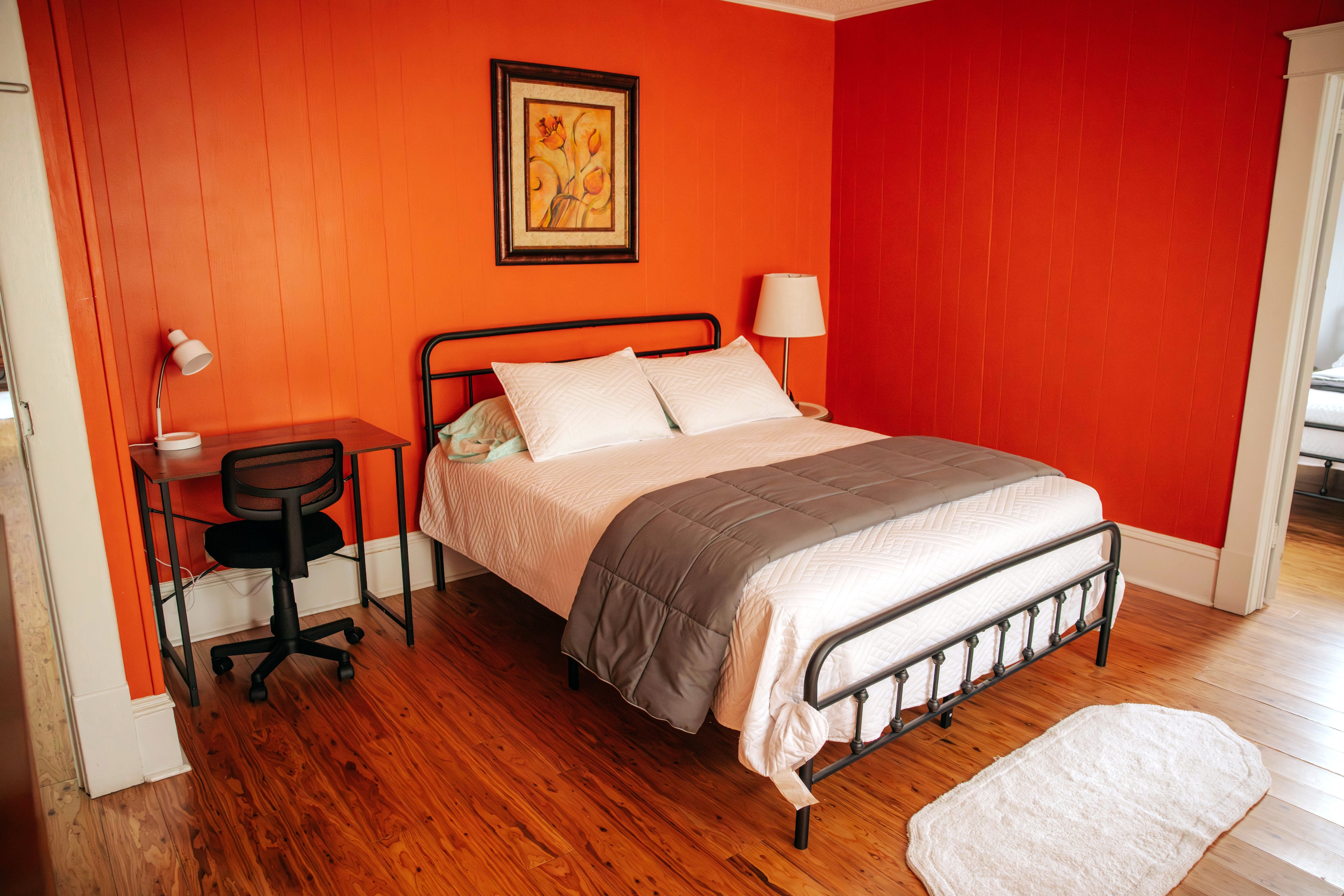 Cozy bedroom with an orange wall, a double bed, a desk with a chair, and wooden flooring.