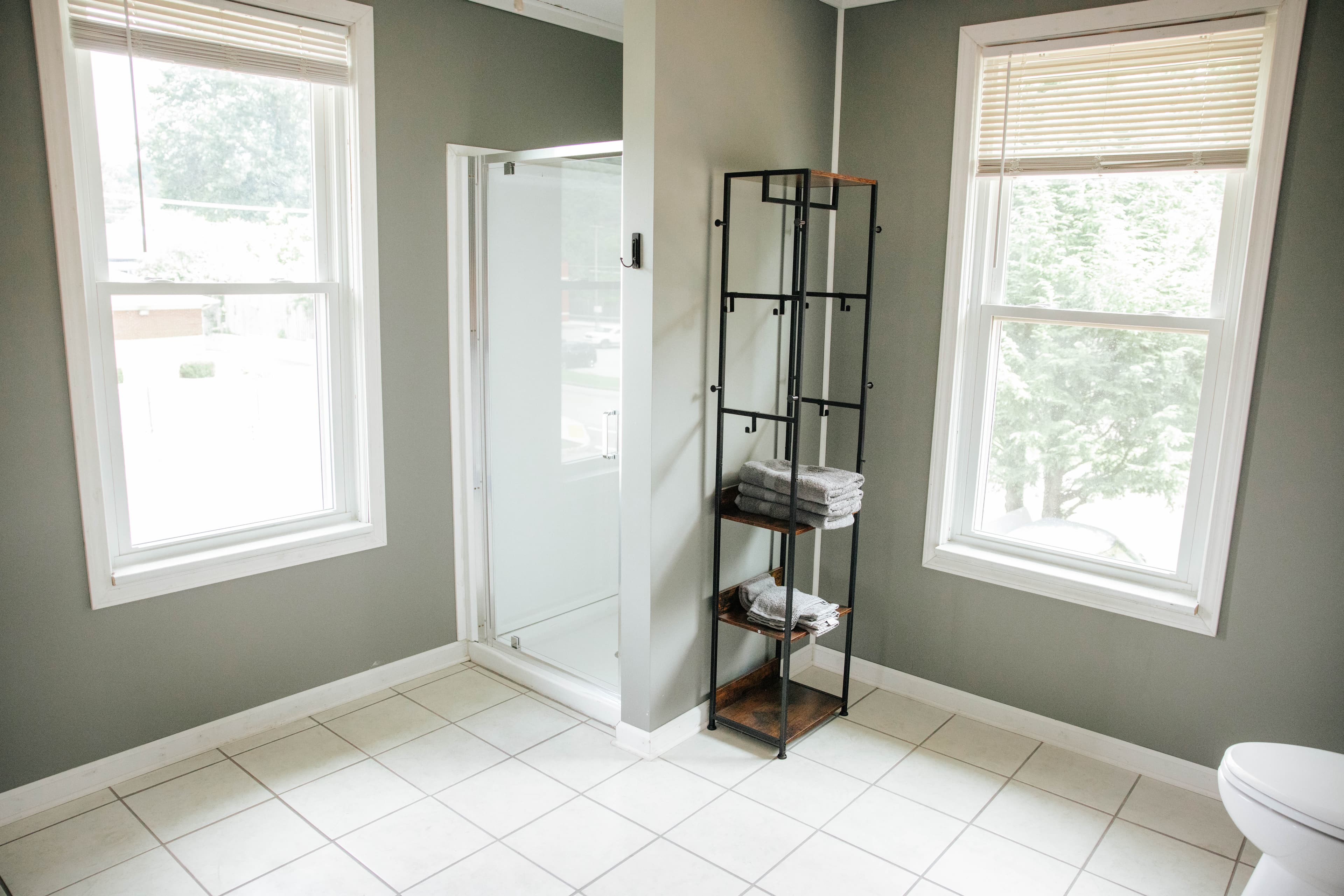 A modern bathroom featuring a glass shower, a shelf with neatly folded towels, and two large windows.