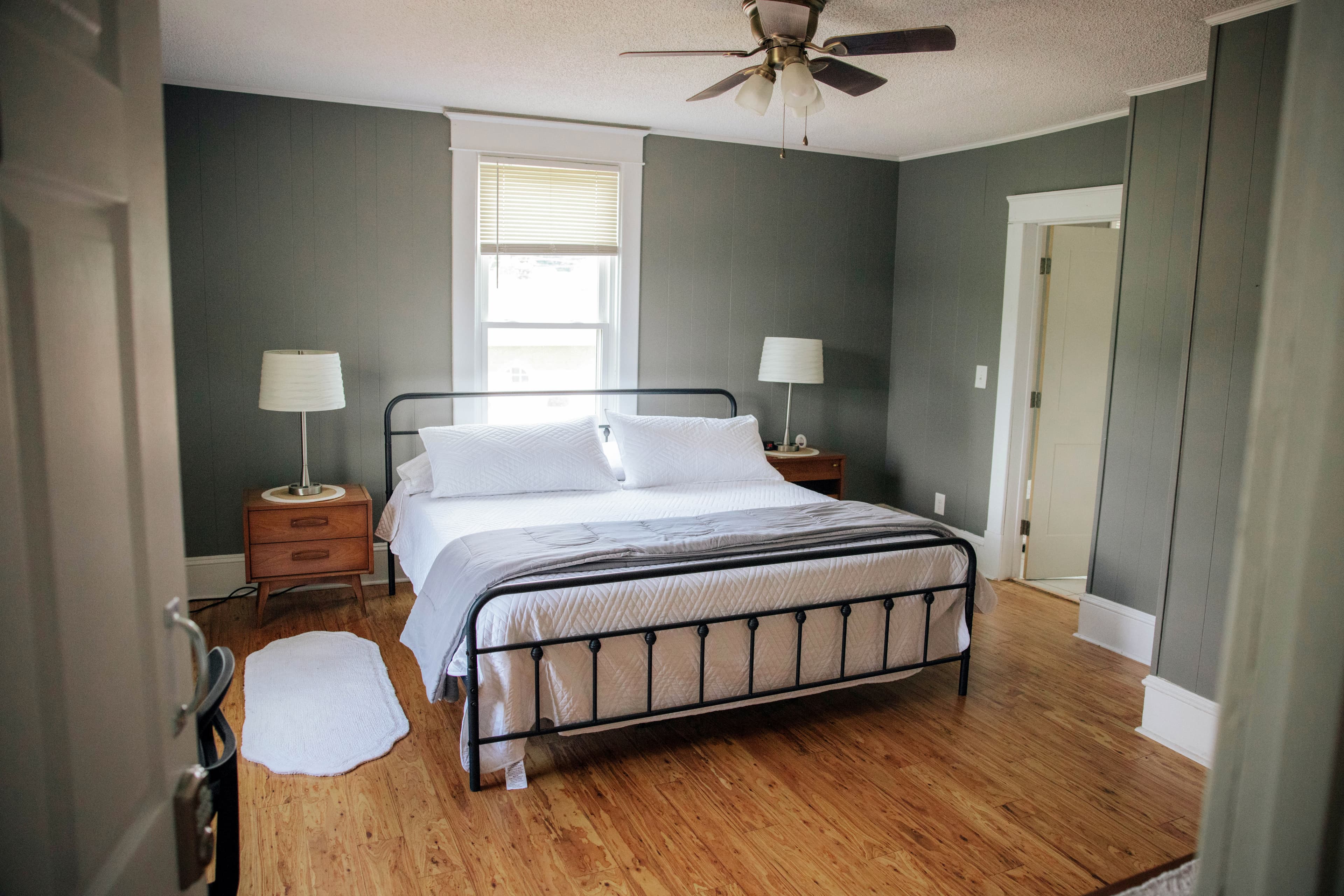 A cozy, well-lit bedroom featuring a black metal bed frame, wooden furniture, and gray walls.