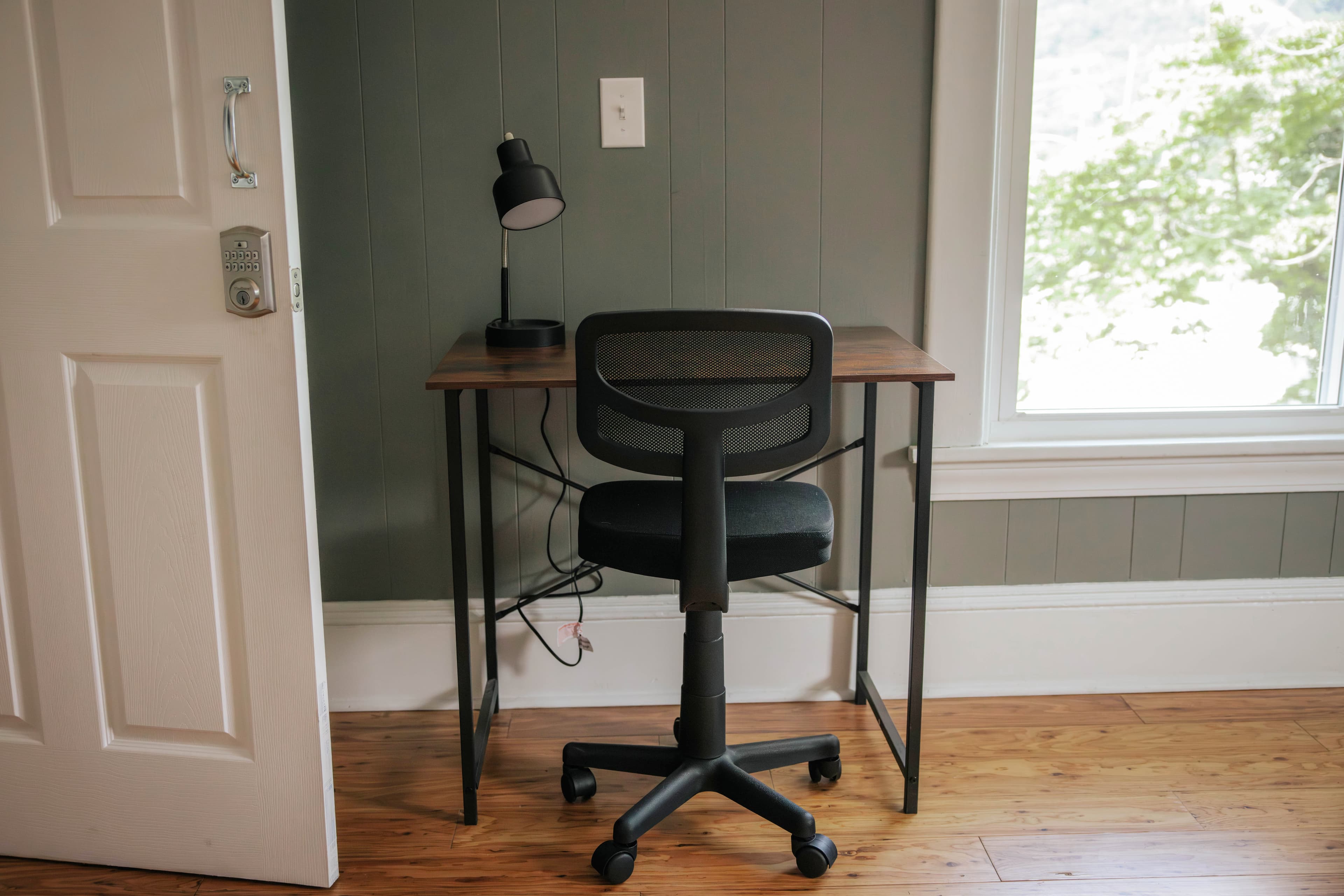 A simple workspace featuring a desk, a chair, and a lamp in a room with green walls.