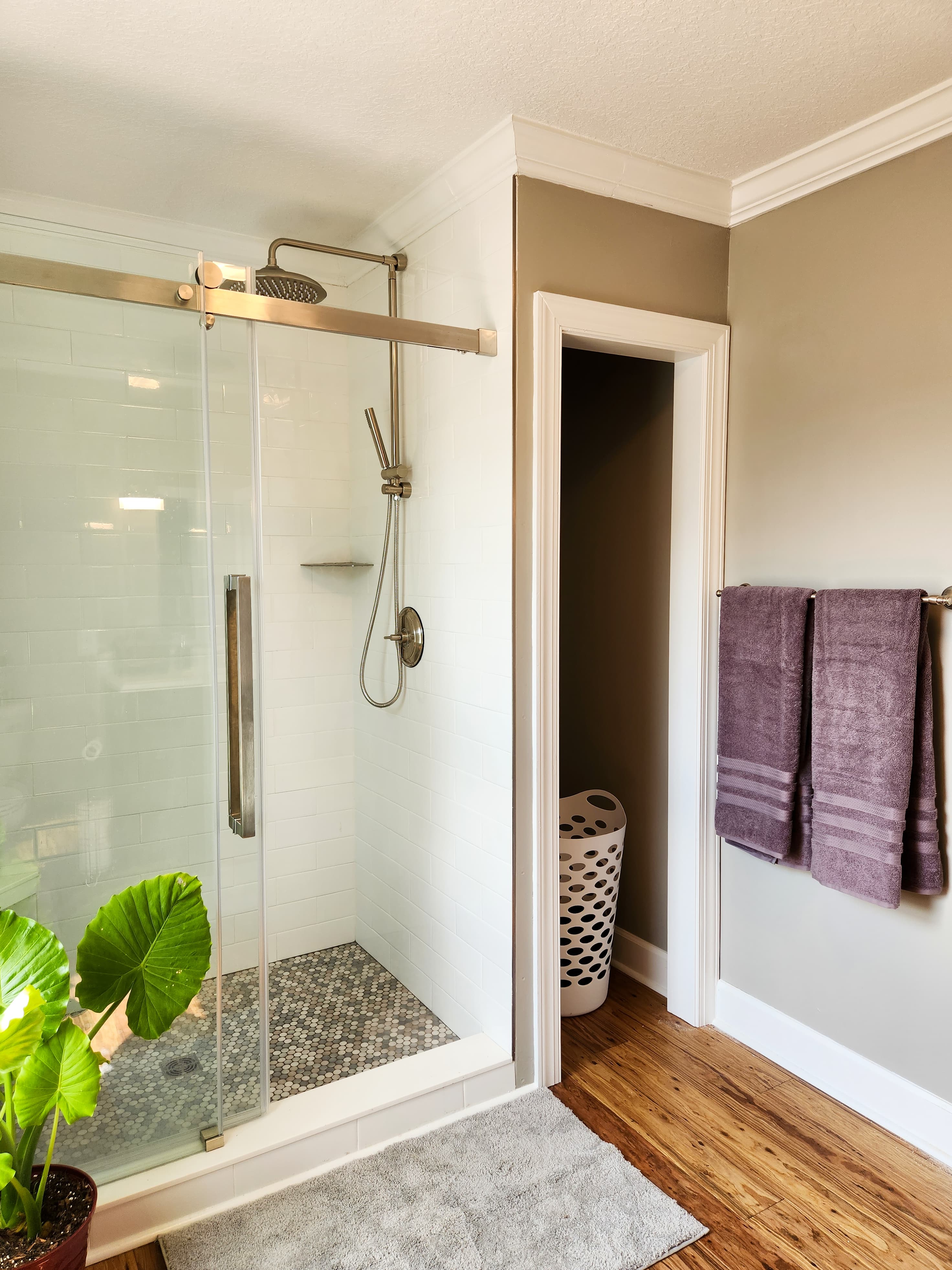 A modern bathroom featuring a glass shower, textured floor tiles, plush towels, and indoor greenery.