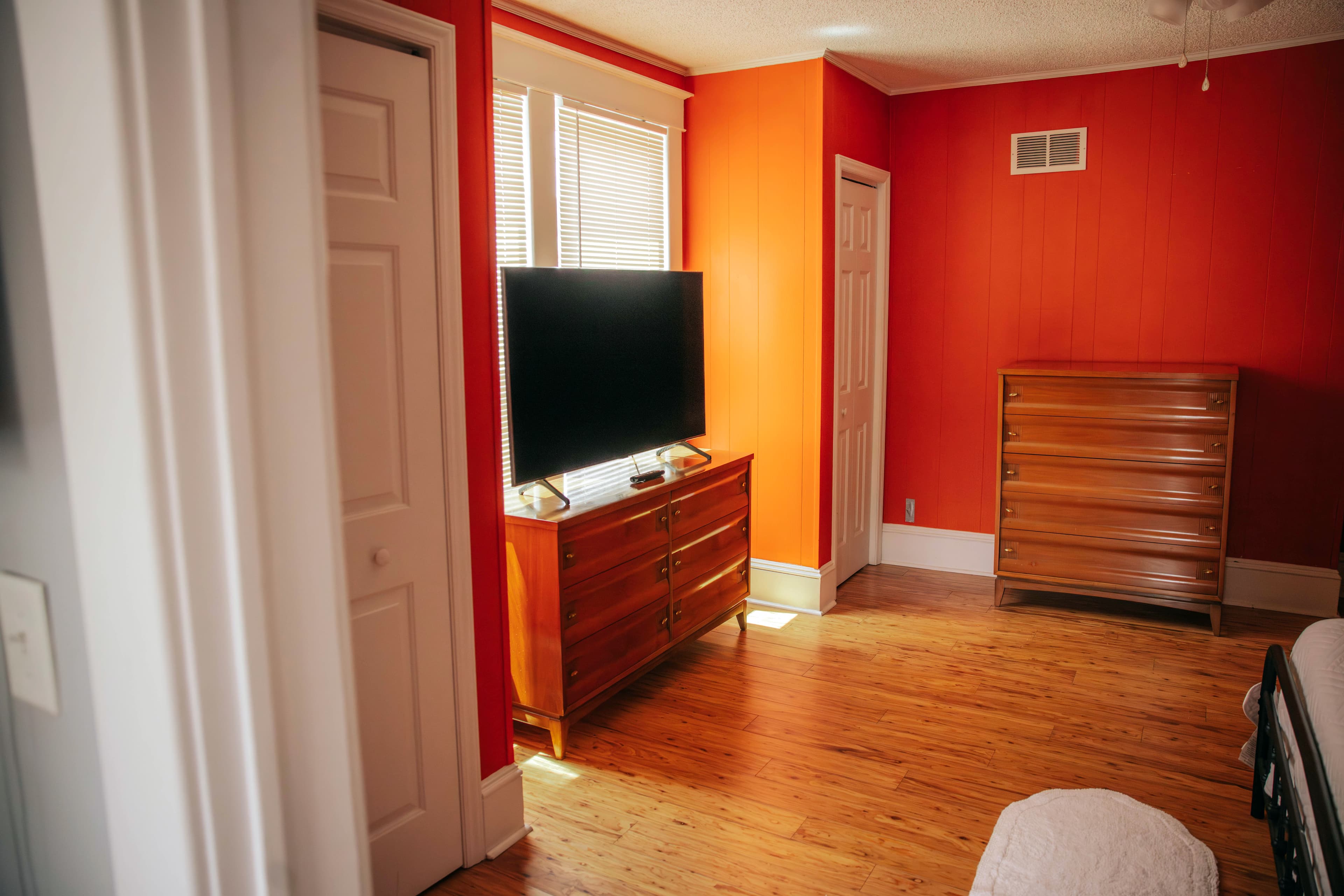 A brightly colored orange bedroom featuring a television and wooden dresser.