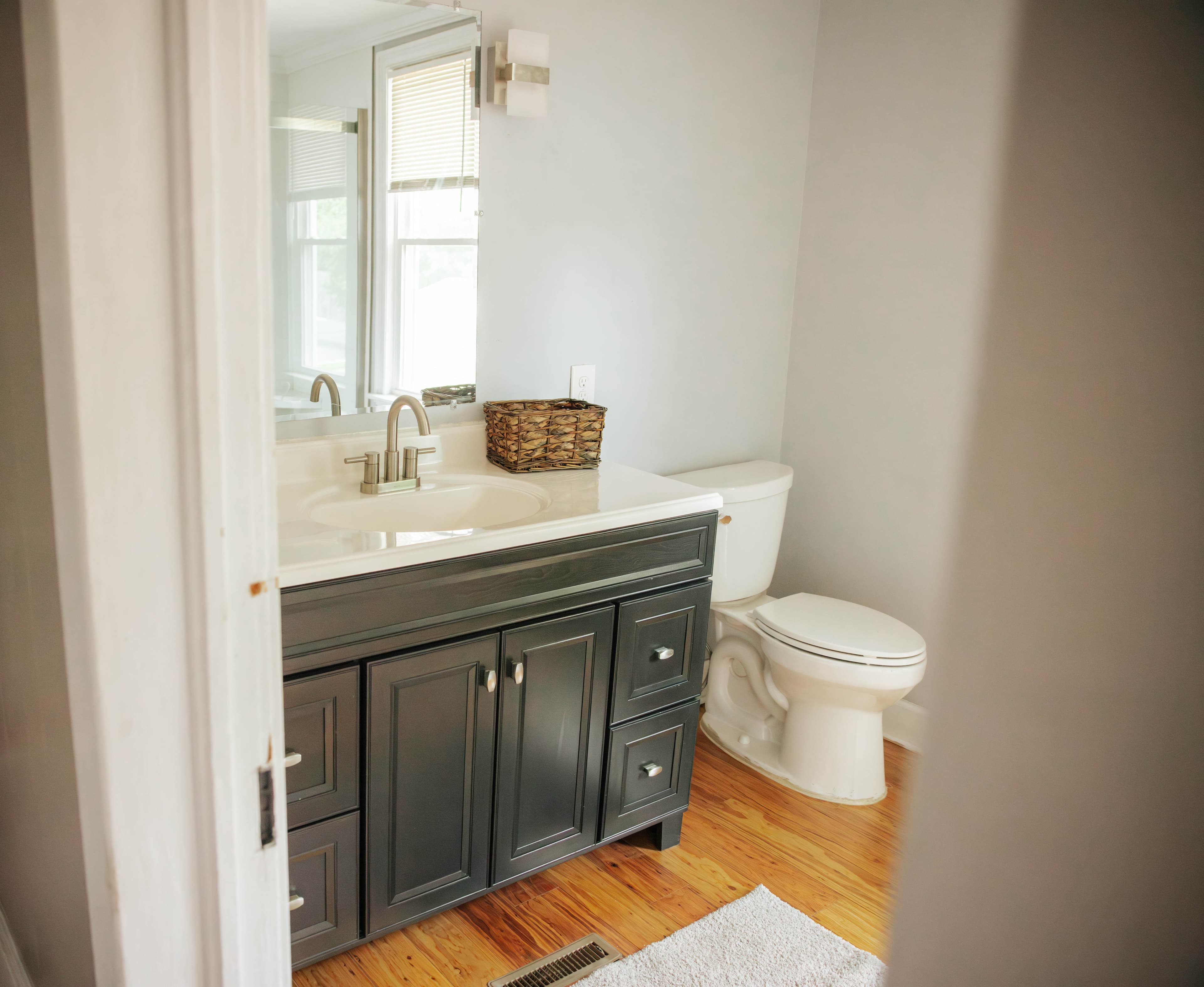 A modern bathroom featuring a dark vanity, white sink, toilet, and natural light from a nearby window.