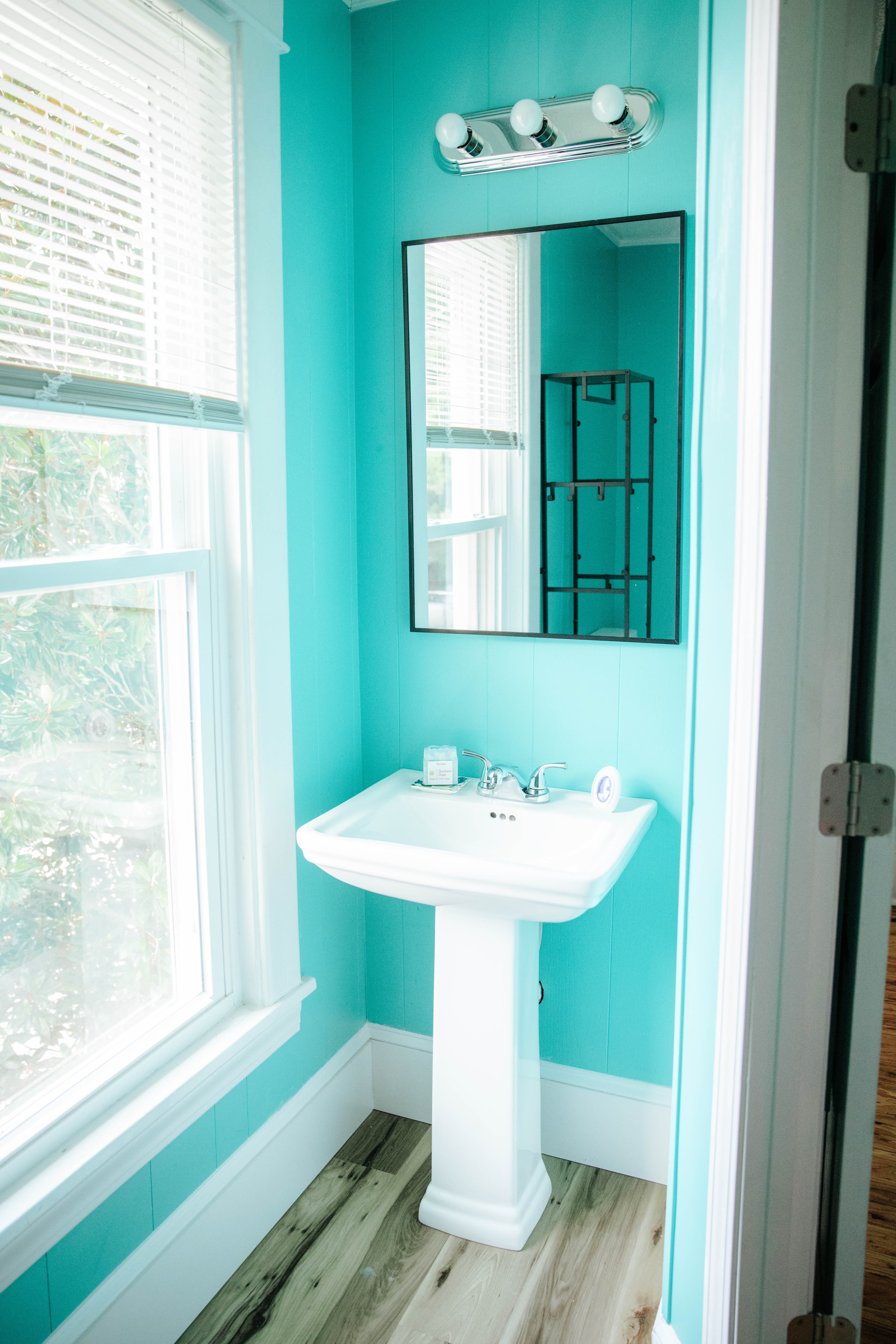 A bright turquoise bathroom featuring a white sink and a large mirror.
