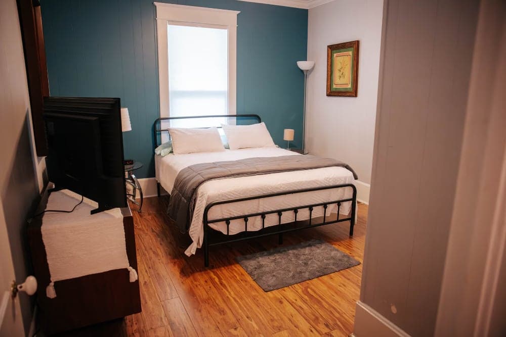 A cozy bedroom featuring a metal bed, wooden flooring, and a blue accent wall.